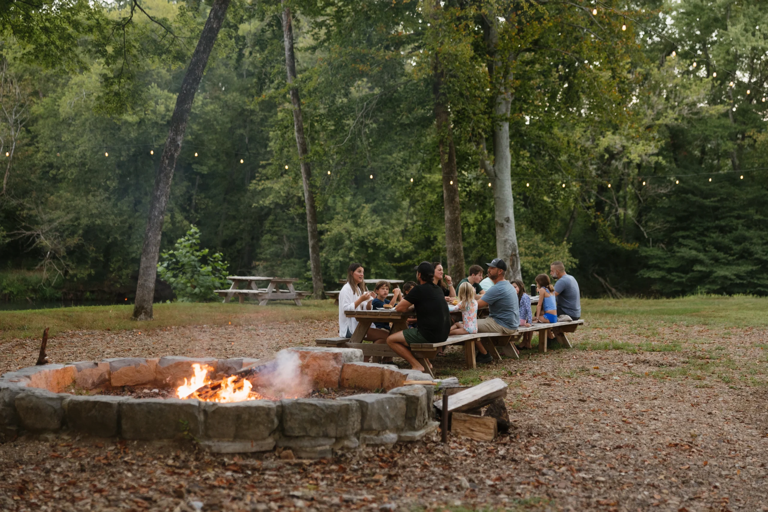 Guests sharing a meal at picnic tables by the fire pit at Riverbend Ranch
